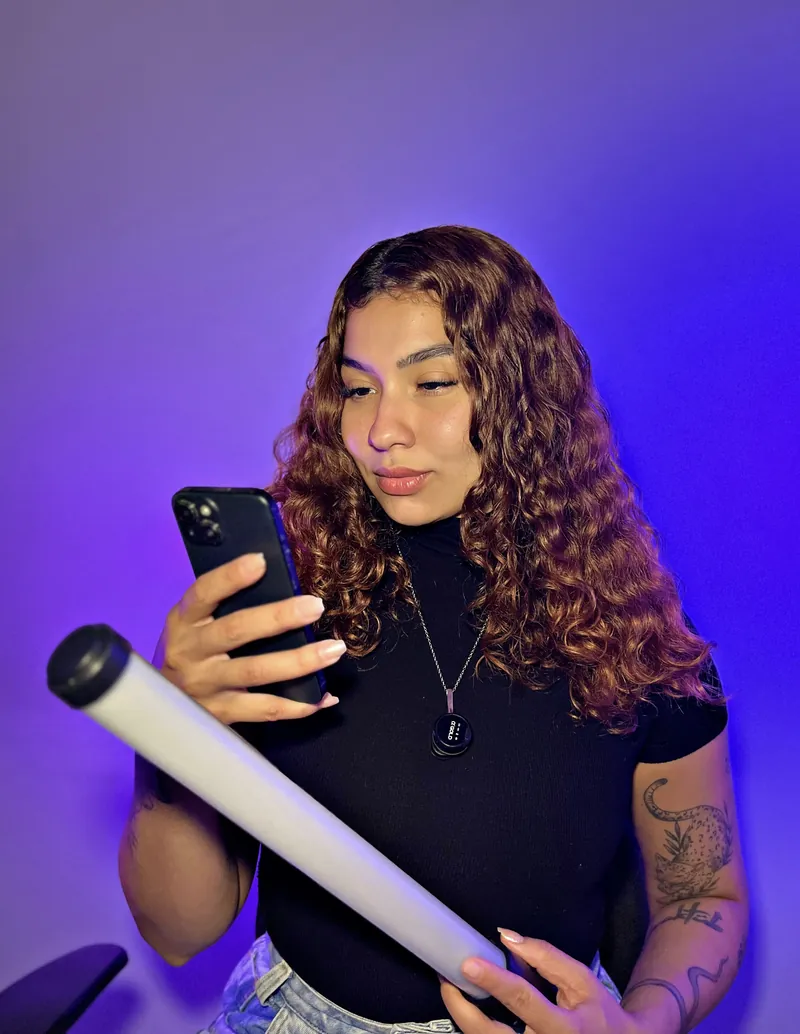 Victoria conferindo o celular com tubo de luz na mão, em estúdio.